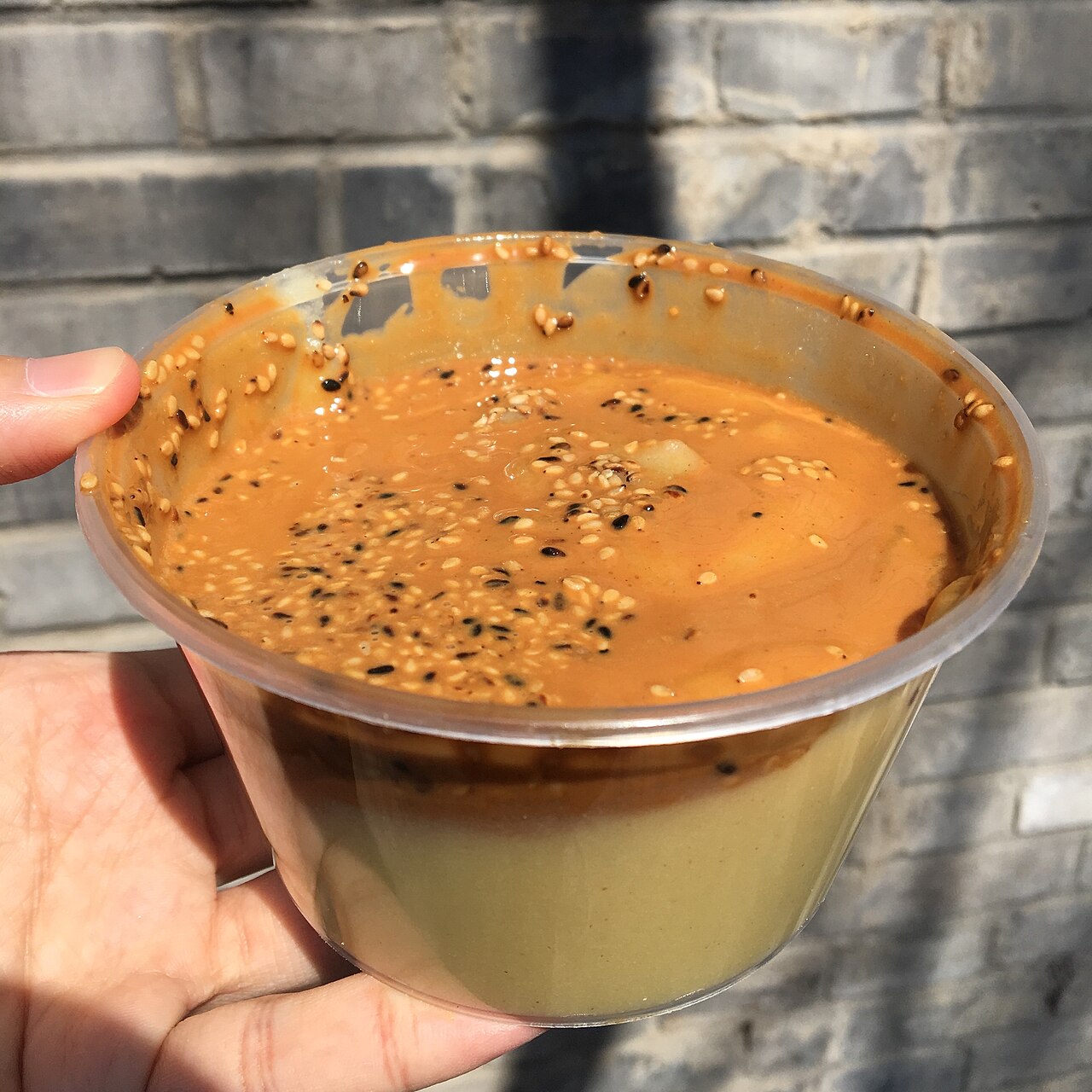 A hand holding Beijing miancha, with sesame paste and sesame seeds on thick millet porridge