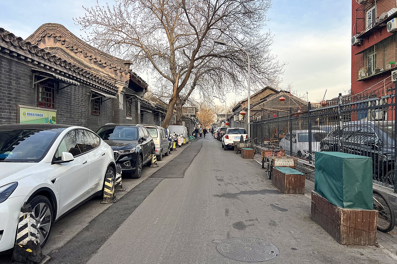 Beijing’s Hangkong Hutong with grey brick courtyard walls, everyday parked cars and a tree-lined lane
