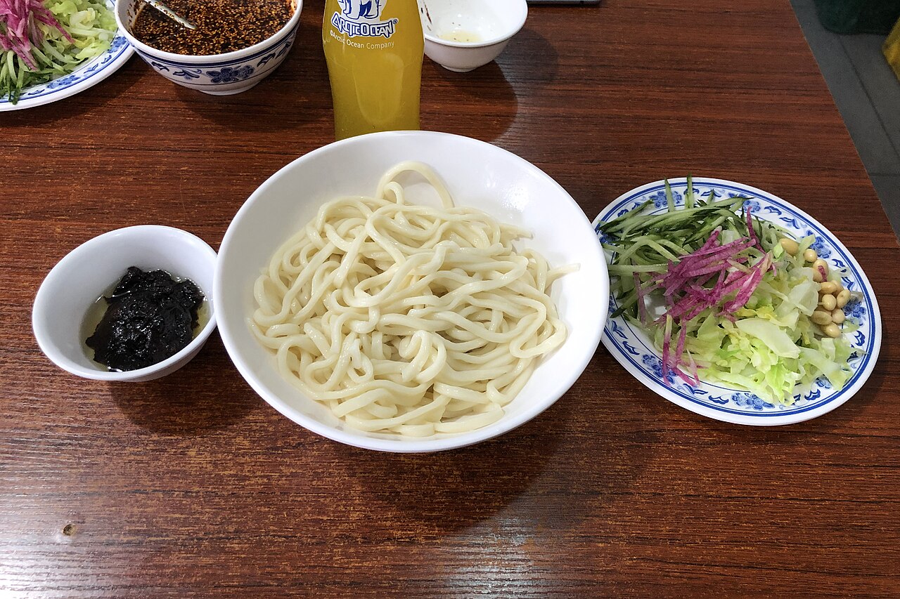 A bowl of Beijing zhajiangmian before mixing, with noodles, soybean-paste sauce and vegetable toppings